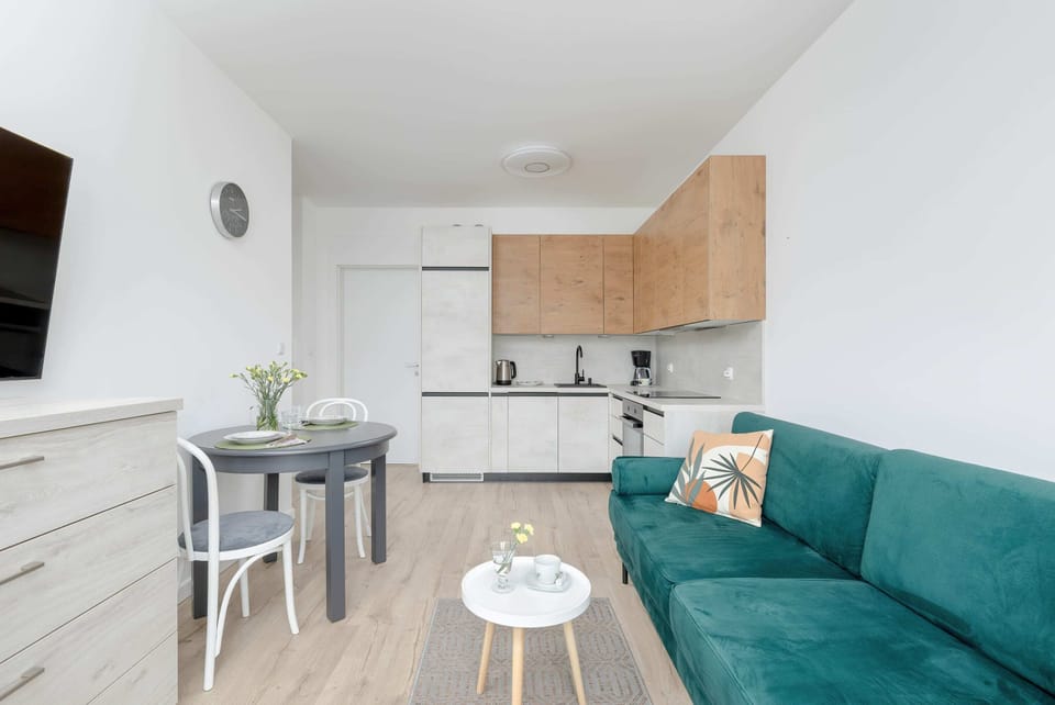 A functional open-plan space with a sofa, dining set, and kitchen. Natural light fills the room through wide windows.