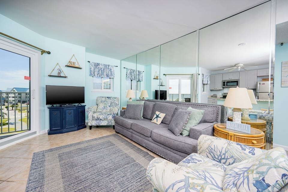 The inviting living area features a cozy sofa, colorful armchairs,and a TV with a lovely view from the balcony