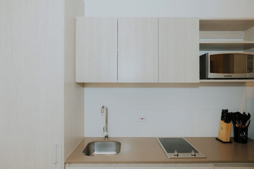 Cocina equipada con estufa, fregadero, microondas y utensilios básicos.