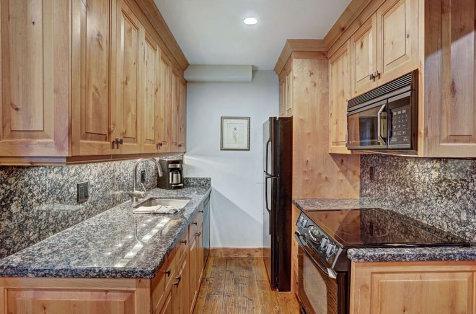 Fully equipped kitchen featuring granite countertops, modern appliances including a microwave and stove, and ample wooden cabinetry for storage. Ideal for preparing home-cooked meals with ease.