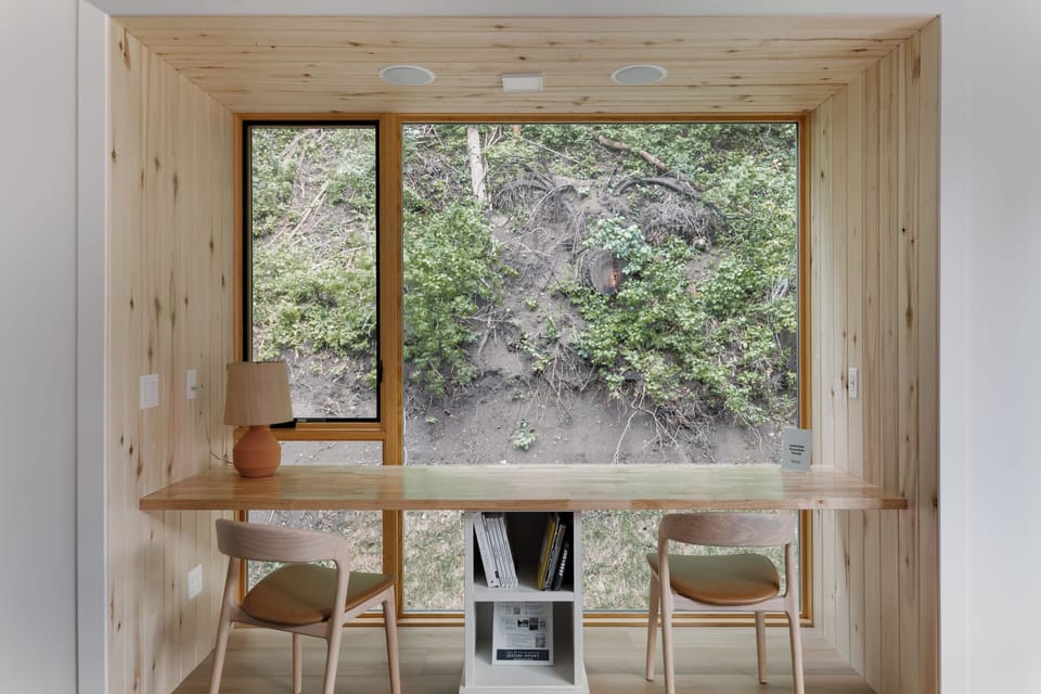 Cozy wood-lined workspace with a built-in desk, forest views, and a quiet tucked-away feel.