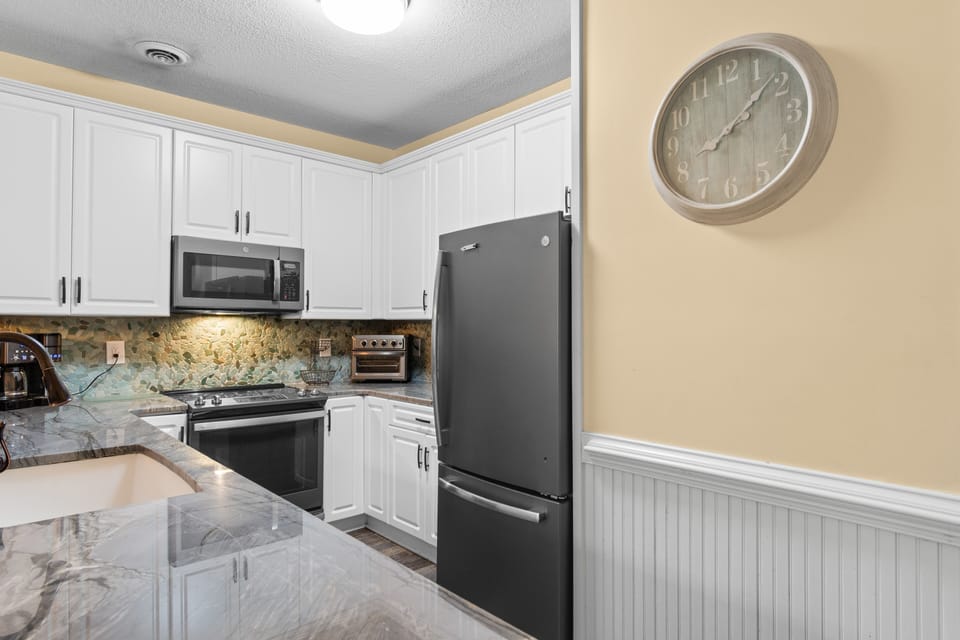 Your fully equipped kitchen features granite countertops, white cabinets, and modern appliances for preparing memorable meals during your stay.