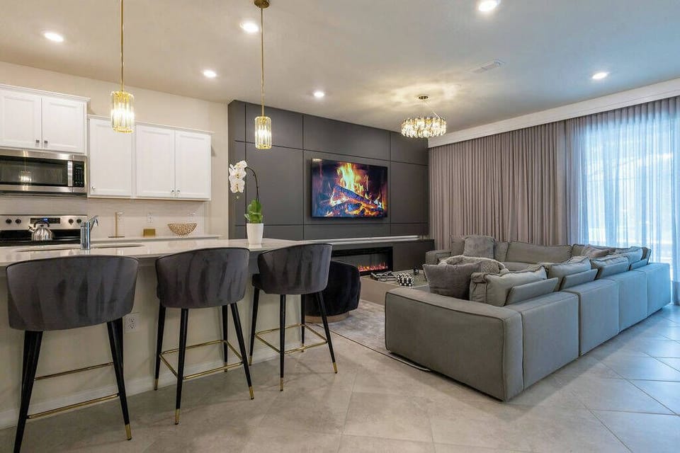 Enjoy a stylish open-concept living area with comfy gray sofas ideal for relaxation. The modern kitchen boasts sleek white cabinets and elegant pendant lighting, while a wall-mounted TV creates a cozy atmosphere for movie nights.