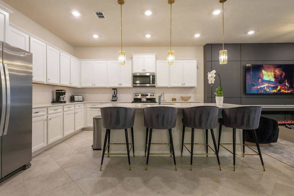 Welcome to this stylish kitchen, featuring sleek white cabinetry and modern appliances. The spacious island with elegant bar stools invites gatherings, while soft lighting creates a warm ambiance for your culinary adventures.
