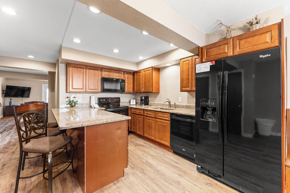 Gather around this fully-equipped kitchen featuring granite countertops, rich wood cabinetry, and modern black appliances for memorable meal preparations.