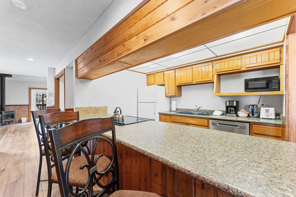 Your fully equipped kitchen awaits with warm wood cabinets, granite counters, and exposed beams creating a cozy mountain retreat atmosphere.