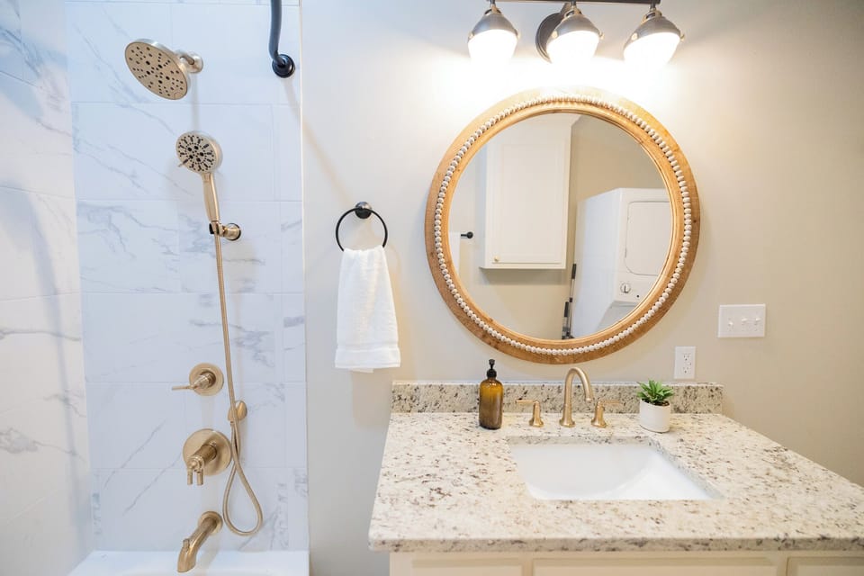 - Bright vanity with a glowing round mirror, granite countertop, and gold accents that pop - Refresh under a dual head shower surrounded by sleek, modern tilework - Stylish space that makes it easy to get ready, unwind, and feel completely at ease