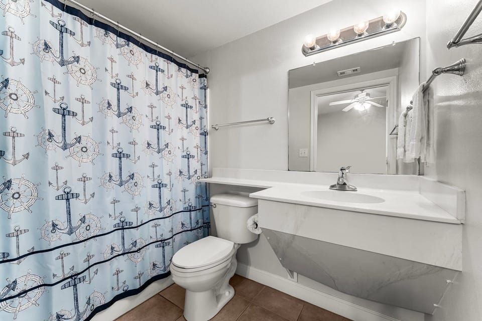 Clean bathroom with nautical-themed shower curtain and ample lighting