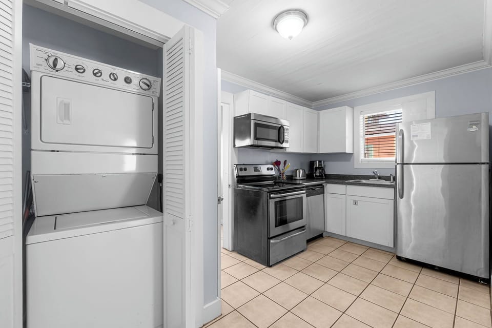 Compact kitchen with stainless steel appliances and a stacked washer and dryer.