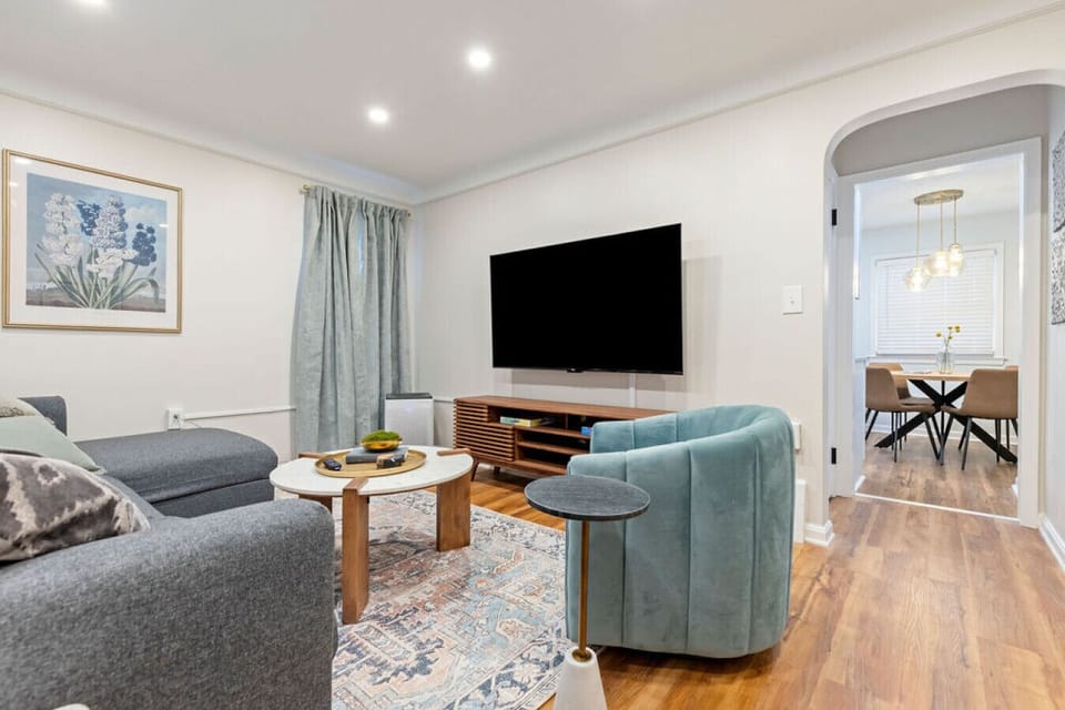 Stylish and cozy living area with a modern aesthetic, featuring plush seating, a large TV, and a peek into the elegant dining space—ideal for relaxing or entertaining.