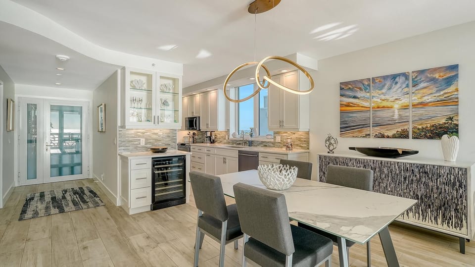 Dining area with marble-top table, gray upholstered chairs, and a modern gold loop chandelier above.