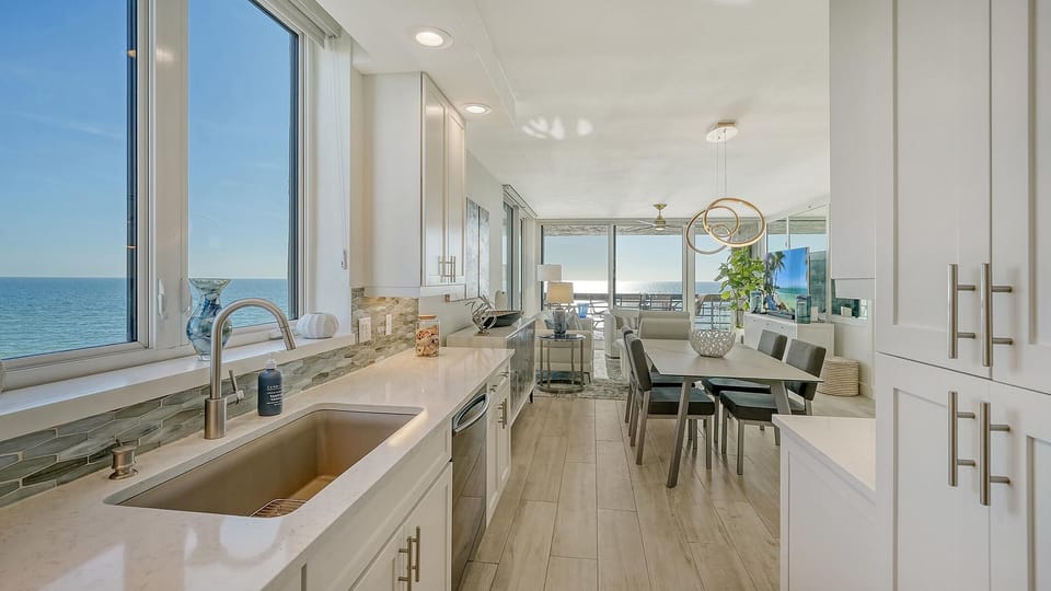 Kitchen features quartz countertops, stainless steel sink and dishwasher, with ocean views through large windows.