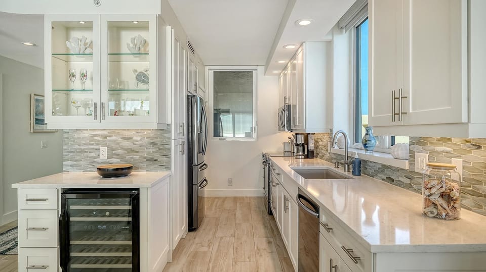 Galley kitchen with quartz countertops, glass-front cabinets, stainless steel appliances, and a textured gray tile backsplash.