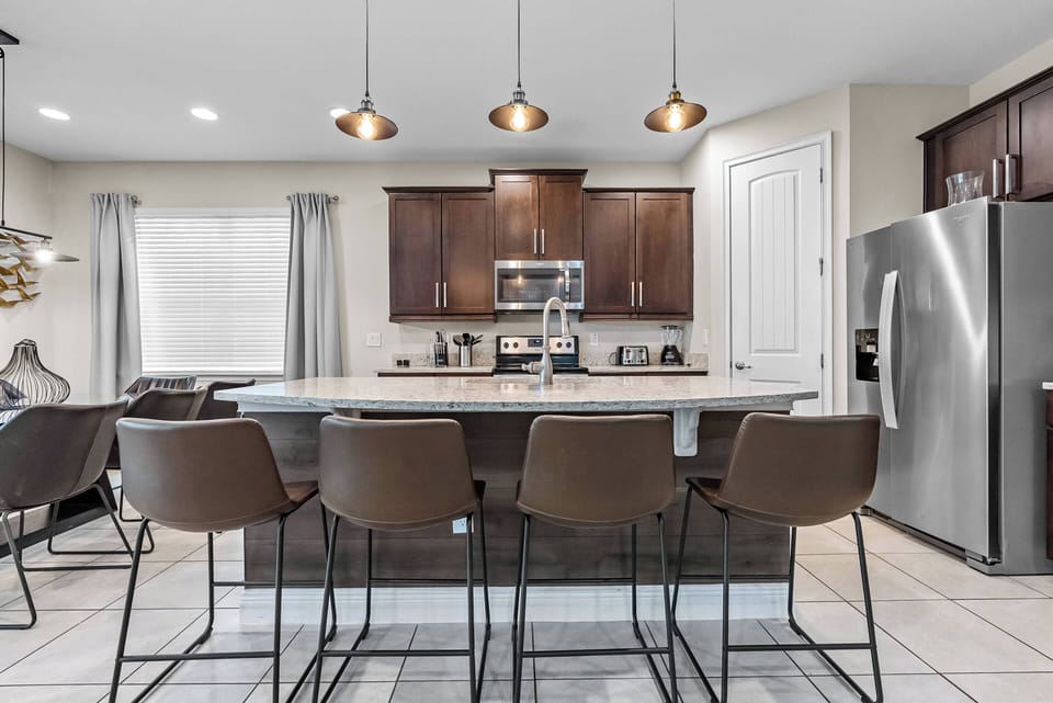 Welcome to this stylish kitchen featuring rich brown cabinetry and sleek stainless steel appliances. Enjoy casual dining at the modern bar under warm pendant lights, perfect for culinary creativity and social gatherings.