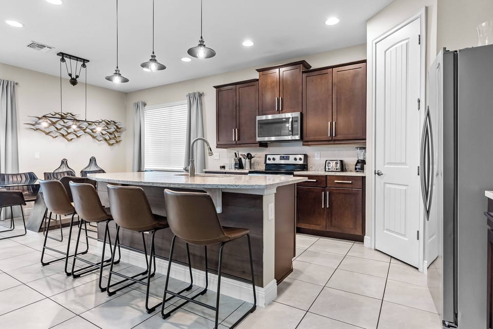 Welcome to this stylish kitchen featuring sleek dark wood cabinets and light countertops. With plenty of seating at the modern bar and bright lighting, it's an ideal spot for morning coffee or meal prep.