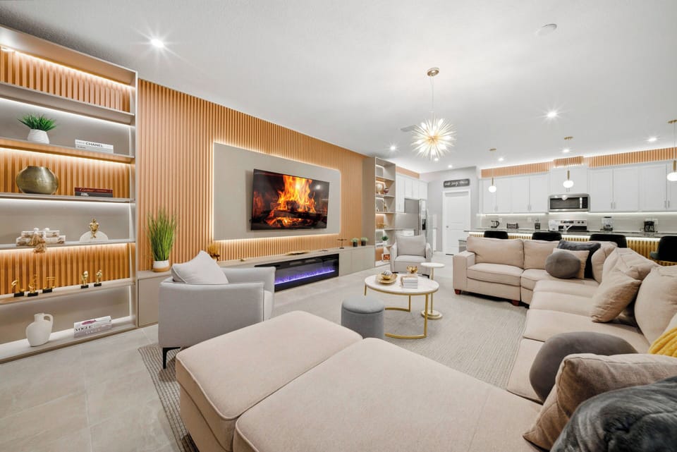 Enjoy the warmth of a cozy living room with soft beige sofas and sleek LED-lit shelving. The modern fireplace enhances comfort, and the open layout effortlessly connects to the kitchen for a welcoming atmosphere.