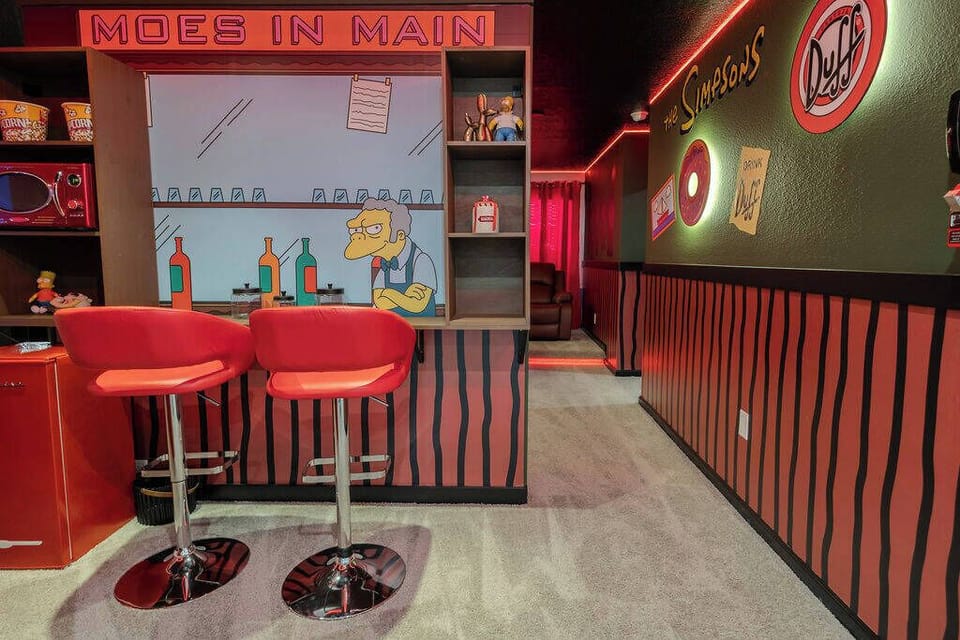 Step into a vibrant bar area featuring sleek red stools and playful wall art that captures a fun, nostalgic vibe. The unique decor and ambient lighting create a lively atmosphere, perfect for relaxing or entertaining with friends.