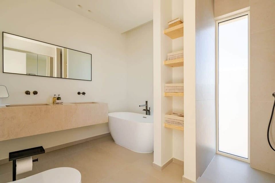 A spa-like retreat featuring a luxurious soaking tub, a spacious shower, and premium Molton Brown toiletries. His-and-hers sinks, a makeup mirror, and a Dyson hairdryer add convenience and elegance to this en-suite sanctuary.