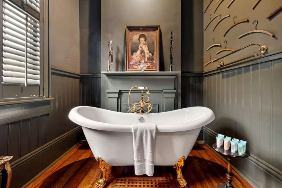 Upstairs bath with a statement claw-foot soaking tub on gilded feet, framed by vintage art and classic shutters.