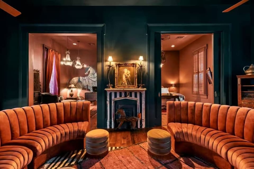 Original fireplace mantels, vintage artwork, and tall windows dressed in black drapery create a moody, sophisticated New Orleans vibe. The double doors on the right is the entry to the first bedroom.