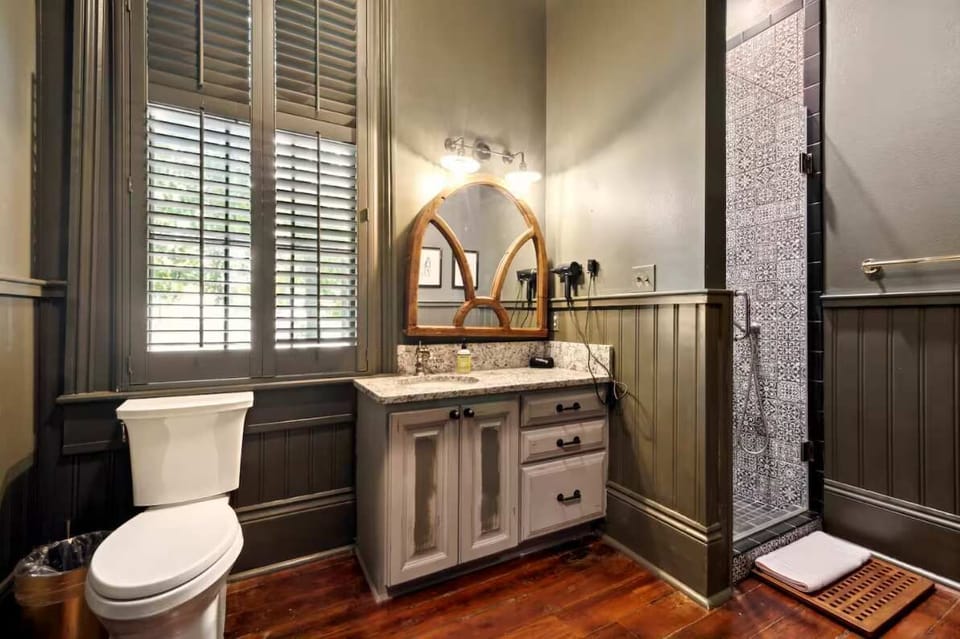 Full first-floor bathroom featuring a patterned-tile standing shower and granite vanity beneath an arched wood mirror.