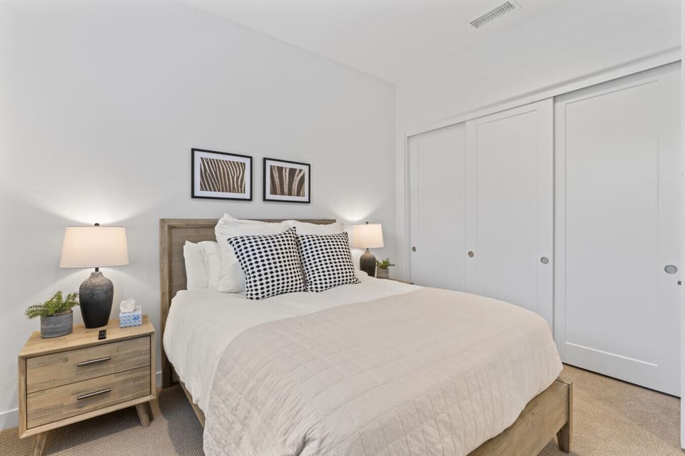Serene bedroom w/ neutral tones, layered pillows & bedside lighting