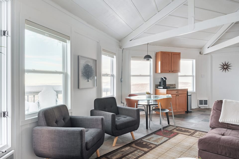 Bright open-concept living and dining space with mountain views, exposed beams, and seating for meals or coffee. Easy flow to the kitchen and deck, perfect for relaxing.