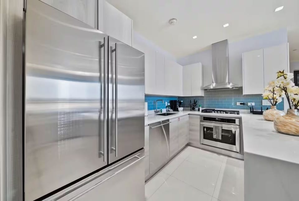 This modern U-shaped kitchen features white cabinets, quartz countertops, and a bold blue backsplash—perfect for cooking, cocktails, or your morning coffee.