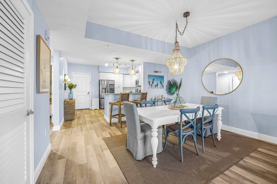 Open dining area with a white table, blue chairs, and a beaded chandelier in a modern coastal style setting.
