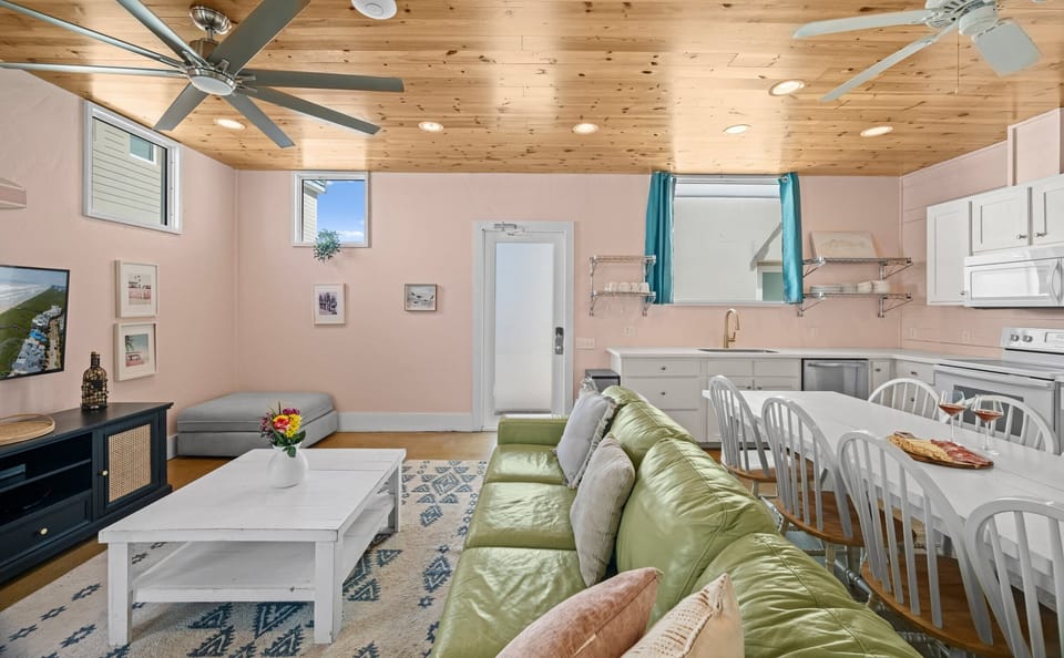 Open Plan — Green Sectional, Gray Daybed, Kitchen & Teal Curtains Under Pine Ceiling