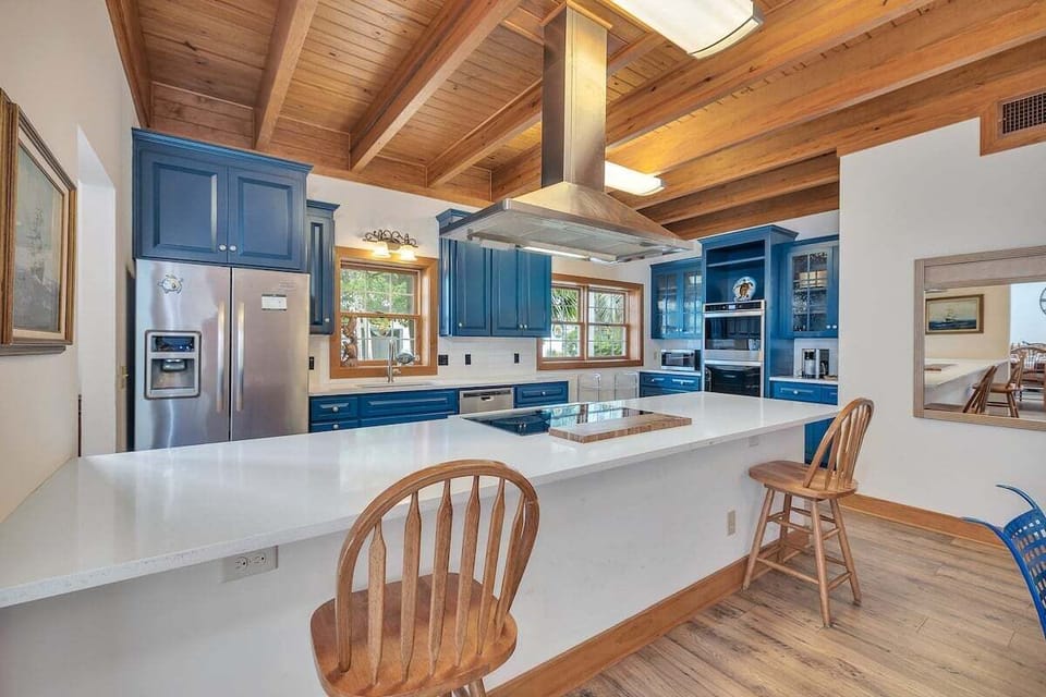Blue kitchen with wood beam ceiling, island, stainless fridge