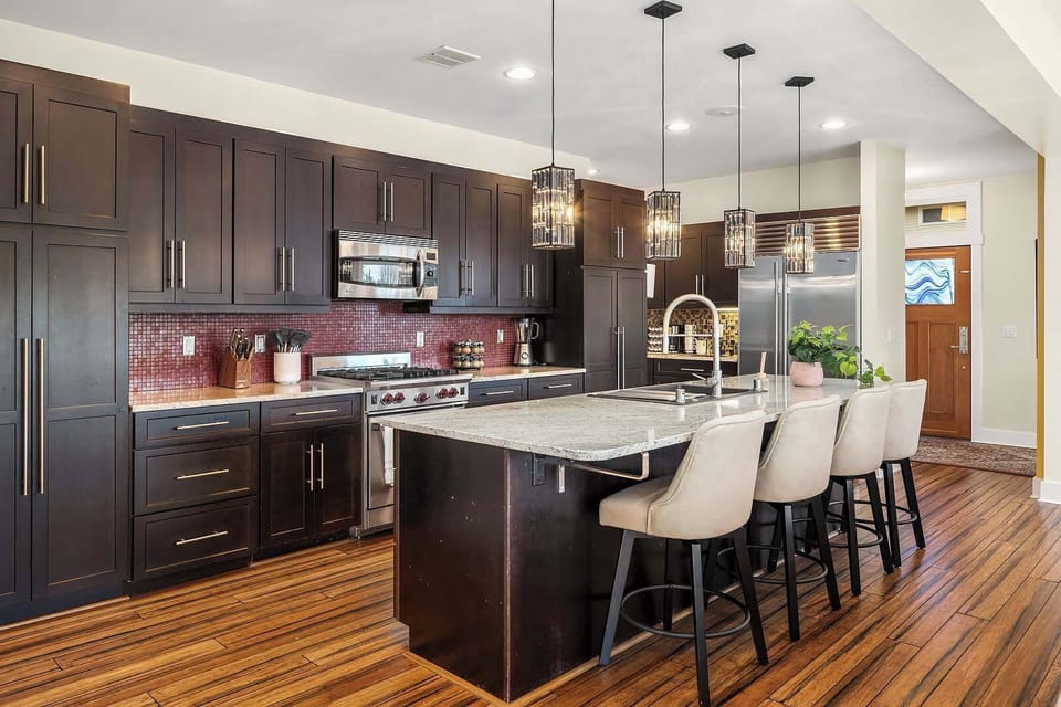
The side view of the kitchen showcases a sleek countertop with seating for four, modern cabinetry, and stainless-steel appliances, blending style and functionality in an open, inviting layout.