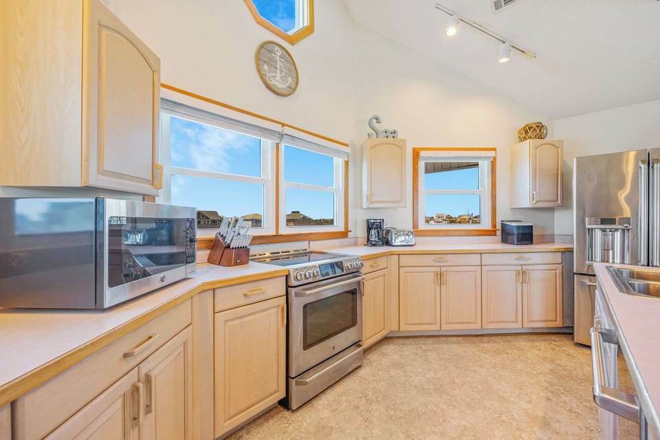 Whip up your favorite meals in this bright, fully equipped kitchen with gleaming appliances and sunny windows framing coastal views—making every morning feel like a fresh start.