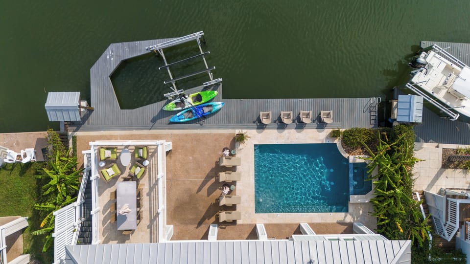 Aerial view of pool, dock & waterfront with kayaks & ample sun-soaked seating.