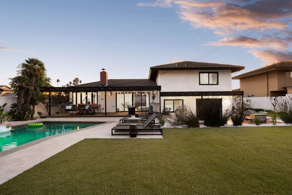 This sprawling two-story retreat unfolds into a lush lawn, glowing pool, and covered patio, all bathed in soft twilight hues. Sleek loungers and string-lit gathering spaces invite you to unwind outdoors from sunset well into the evening.