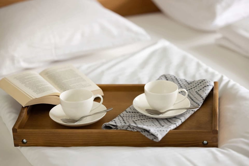 A cozy setup featuring a tray with coffee cups and pastries, perfect for a relaxing morning in bed.