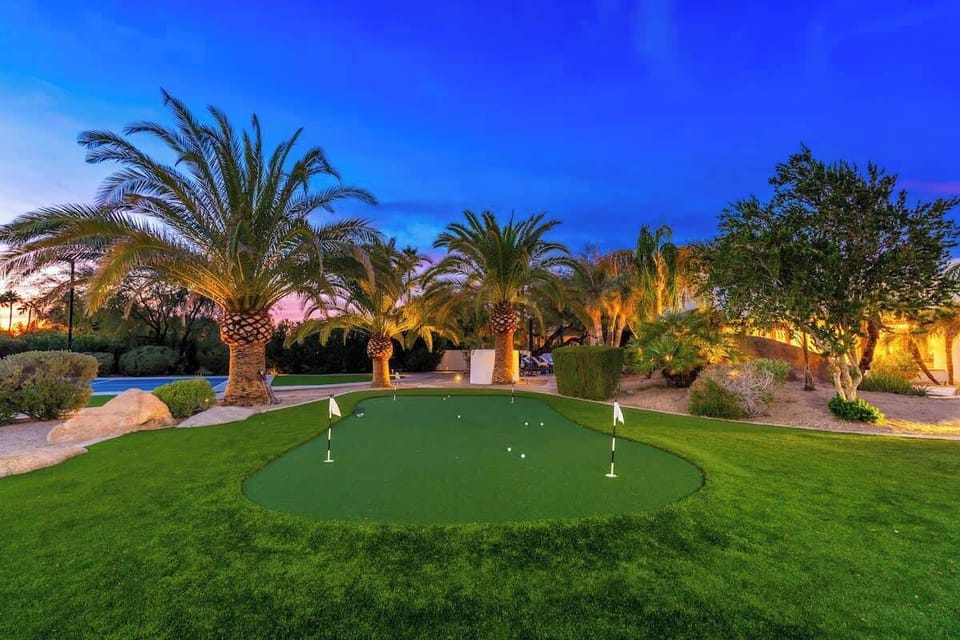 The property features a private putting green surrounded by palm trees and lush gardens, lit beautifully as evening descends. Perfect for practicing your short game under warm ambient lighting.
