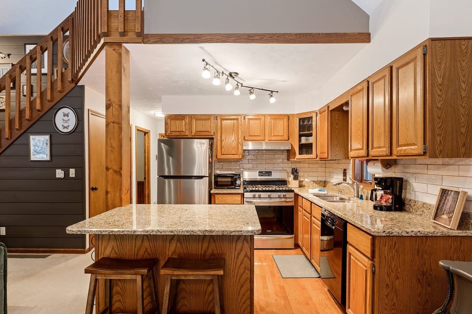 Spacious kitchen w/ rich wood cabinetry, island seating & stainless steel appliances