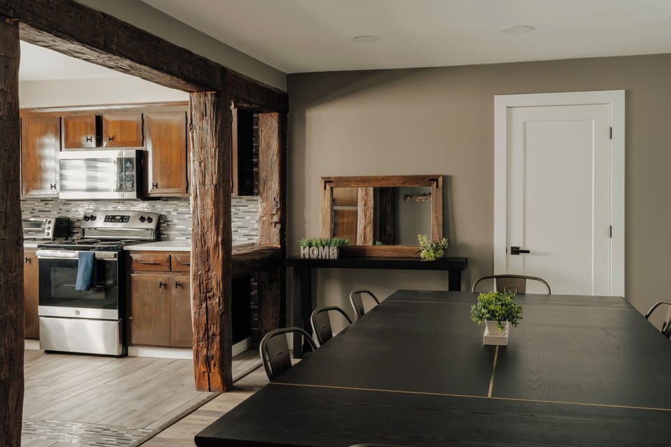 Gather everyone at this long black table, rustic wood beams framing the open pass into the kitchen. A mirrored console nearby adds a nice touch, with a hallway door close by for coming and going.