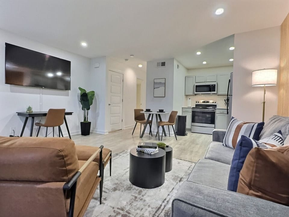 Bright and airy living area in this furnished apartment with comfortable seating, a TV, and a workspace, perfect for relaxing or staying productive.