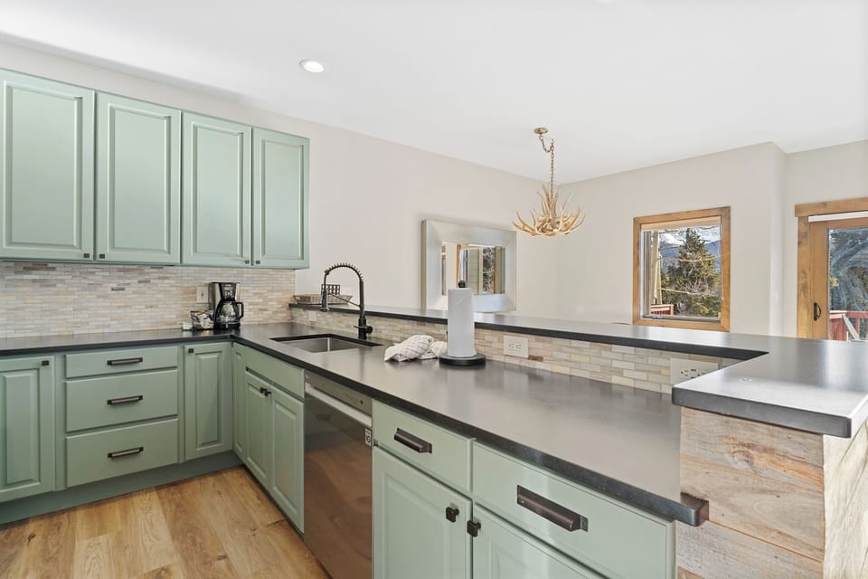 Your chef-worthy kitchen awaits with sage green cabinetry, spacious countertops, and mountain views streaming through warm wood-framed windows.