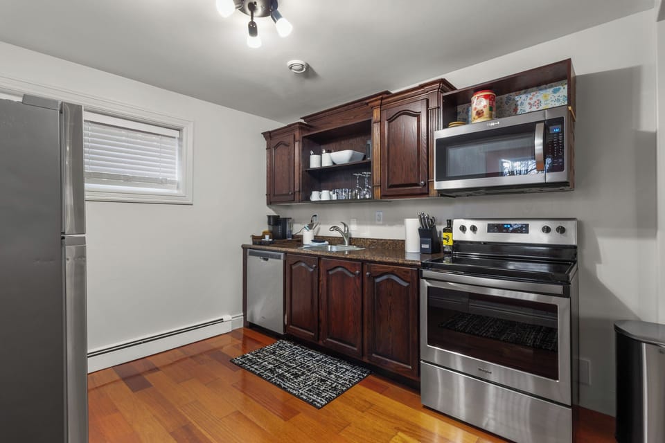 Modern kitchen featuring stainless steel appliances, dark wooden cabinets, and a cozy area rug. Perfect for cooking and enjoying meals during your stay.