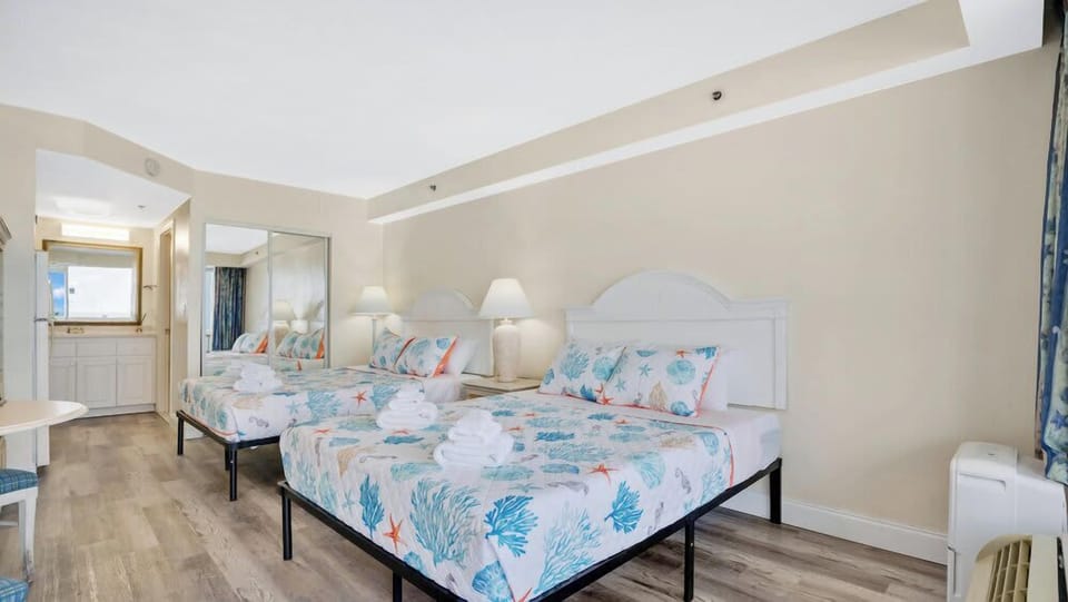 Bright room with two beds featuring ocean-themed bedding and a modern wood floor.