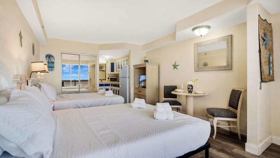 Cozy studio with two beds and a small dining area featuring ocean views through sliding glass doors.