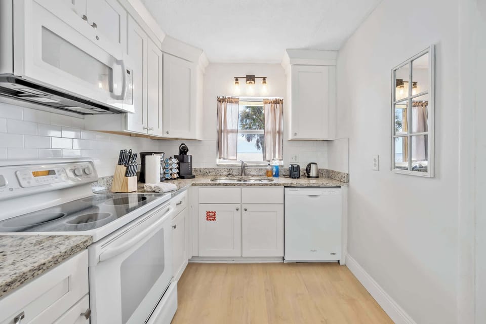 Bright kitchen with white cabinetry and a window view of palm trees.