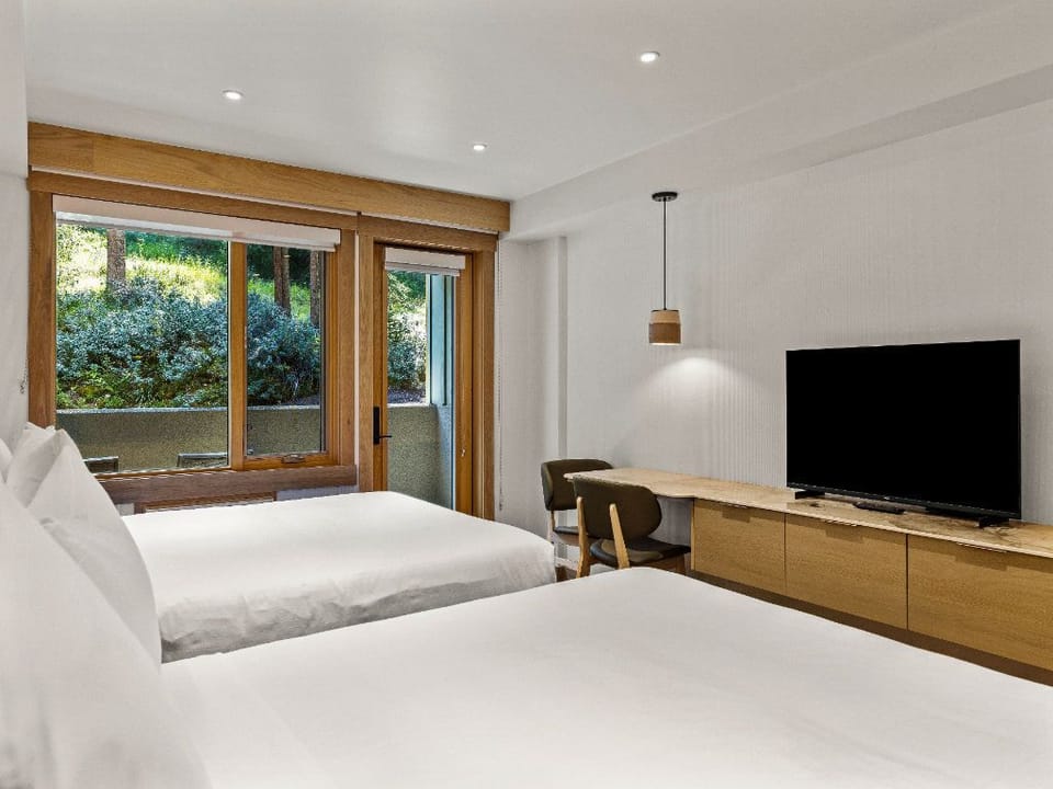 A bright and modern room featuring plush beds, a sleek entertainment setup, and large windows framing serene outdoor views.