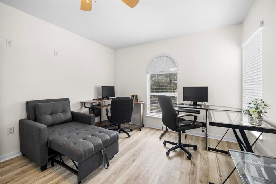 Work area complete with three desks, two monitors, ergonomic work chairs, and plenty of natural light.