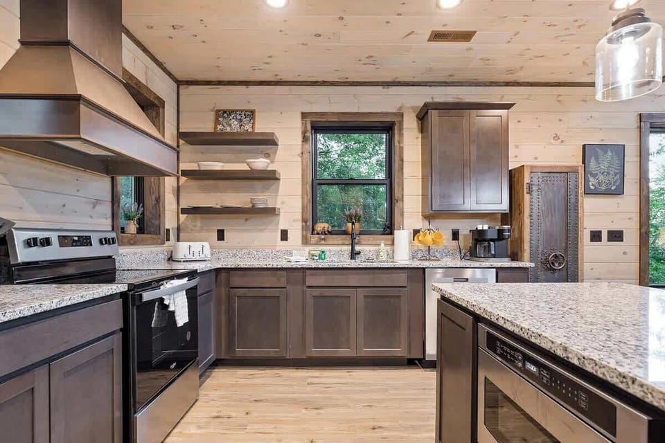 Modern kitchen with granite countertops and dark wood cabinetry overlooking a wooded view.