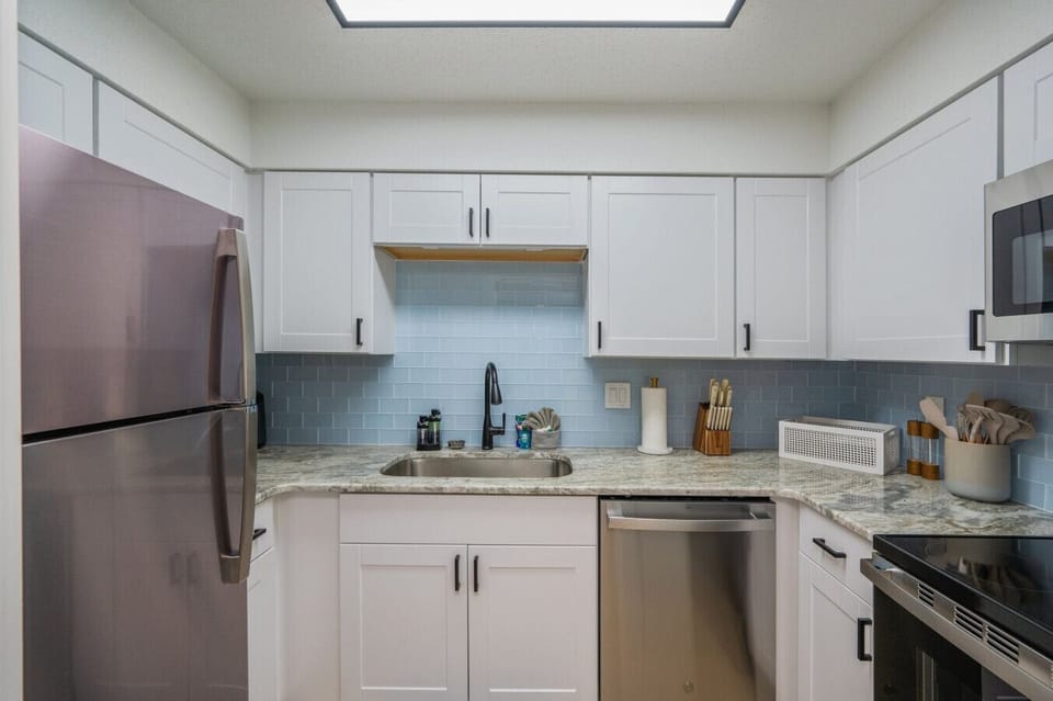 Fully equipped kitchen with fridge, sink, and modern white cabinets.