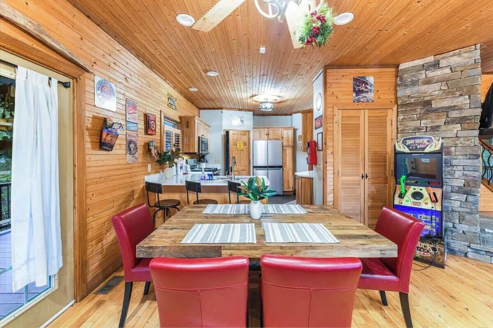 Rustic dining area with red chairs and a game machine near the stone fireplace.